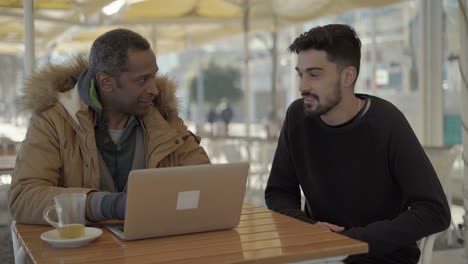 multiethnic men talking and using laptop in cafe