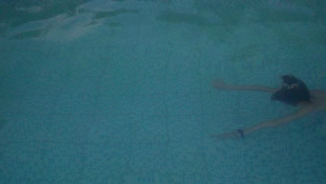 a beautiful slim young woman in a swimsuit swims underwater in an outdoor swimming pool