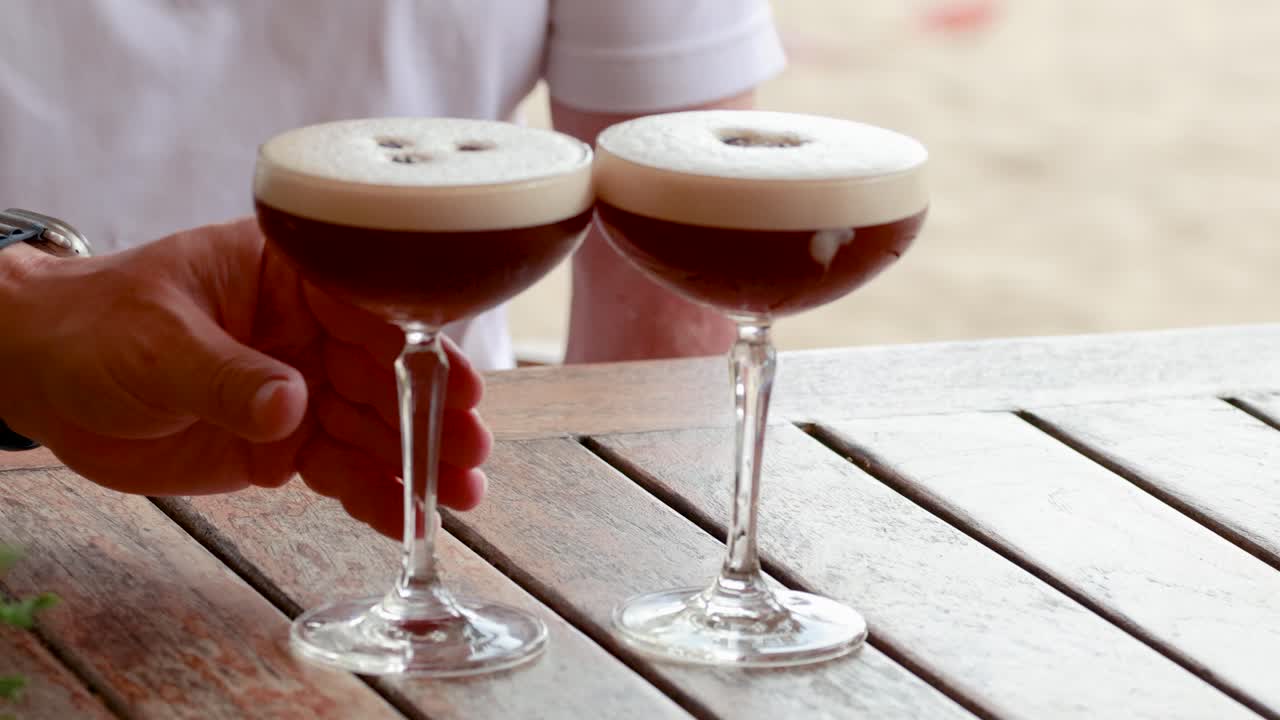Two people toast with espresso martinis at a beachside table in Phuket, Thailand, under natural lighting