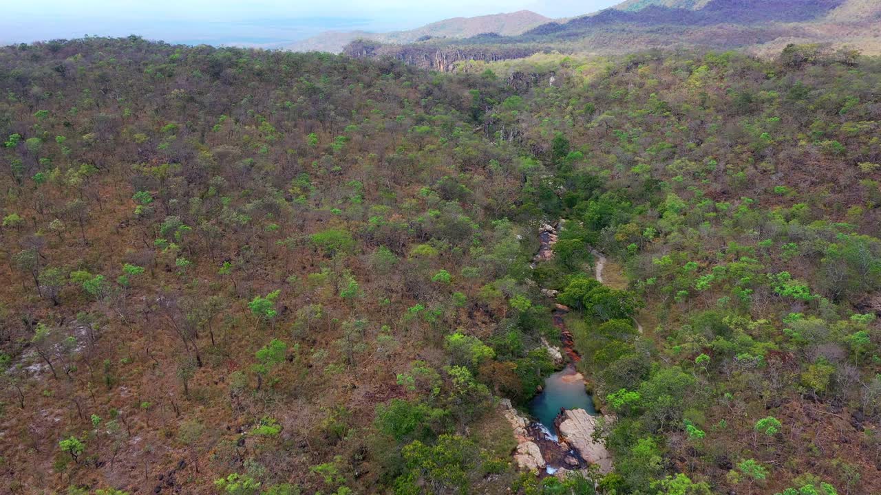 Drone che avanza seguendo un limpido corso d'acqua Canjica e mentre attraversa pozze di roccia arrotondate e brevi cascate, la galleria di alberi più verdi nelle colline del Cerrado, Chapada dos Veadeiros, Goiás, Brasile