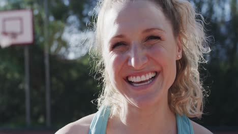 portrait of happy caucasian female basketball player on sunny court, in slow motion