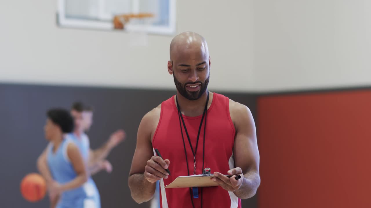 retrato de un feliz entrenador de baloncesto biracial en una cancha cubierta, en cámara lenta