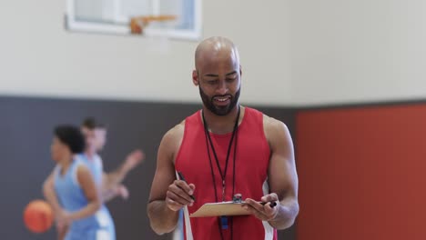 portrait of happy male biracial basketball coach in indoor court, in slow motion