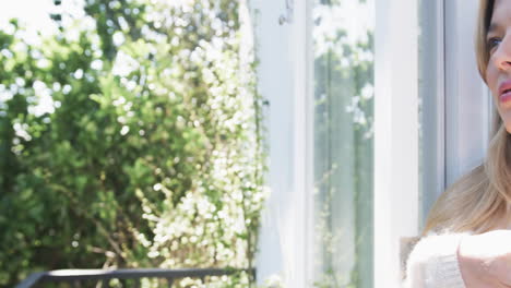 Thoughtful-biracial-woman-looking-through-window-at-home,-slow-motion