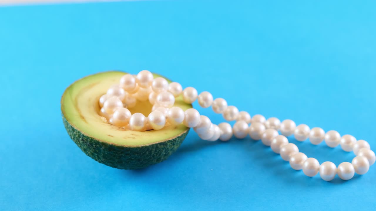 medio fruto de aguacate fresco con perlas en fondo azul. diseño de alimentos de moda