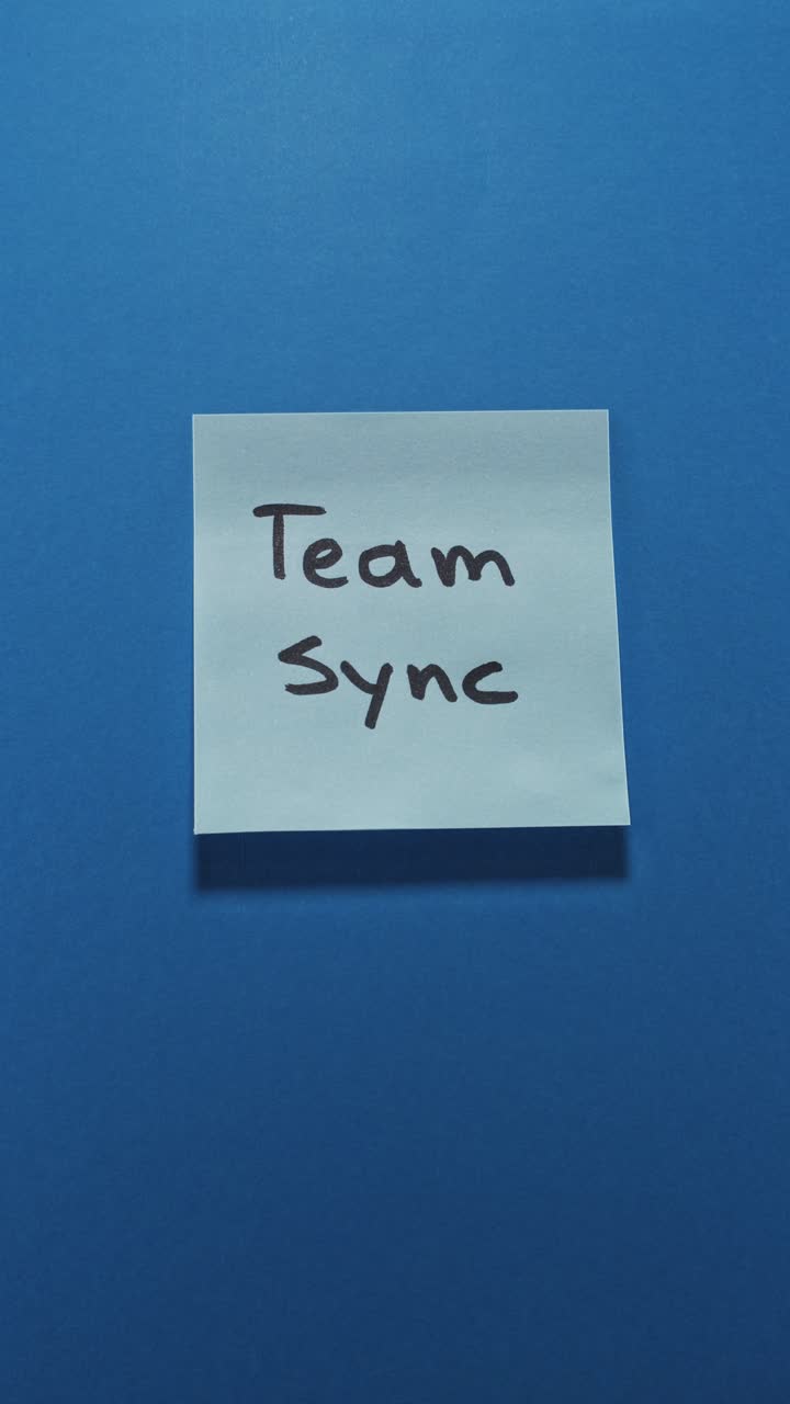 Hands posting Team Sync sticky note on blue wall, portraying teamwork