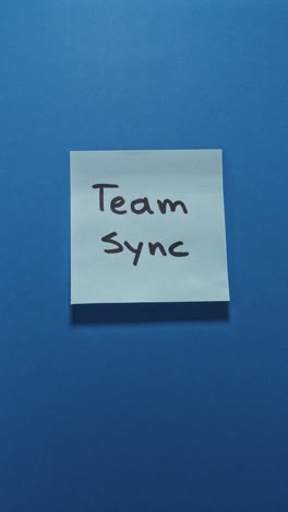 hands posting team sync sticky note on blue wall, portraying teamwork