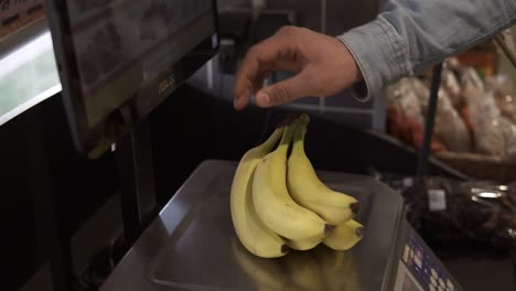 estilo de vida saludable y comida natural. primer plano de la mano de un hombre caucásico pesando un montón de plátanos, poner una etiqueta adhesiva. un tipo vegetariano compra una fruta amarilla