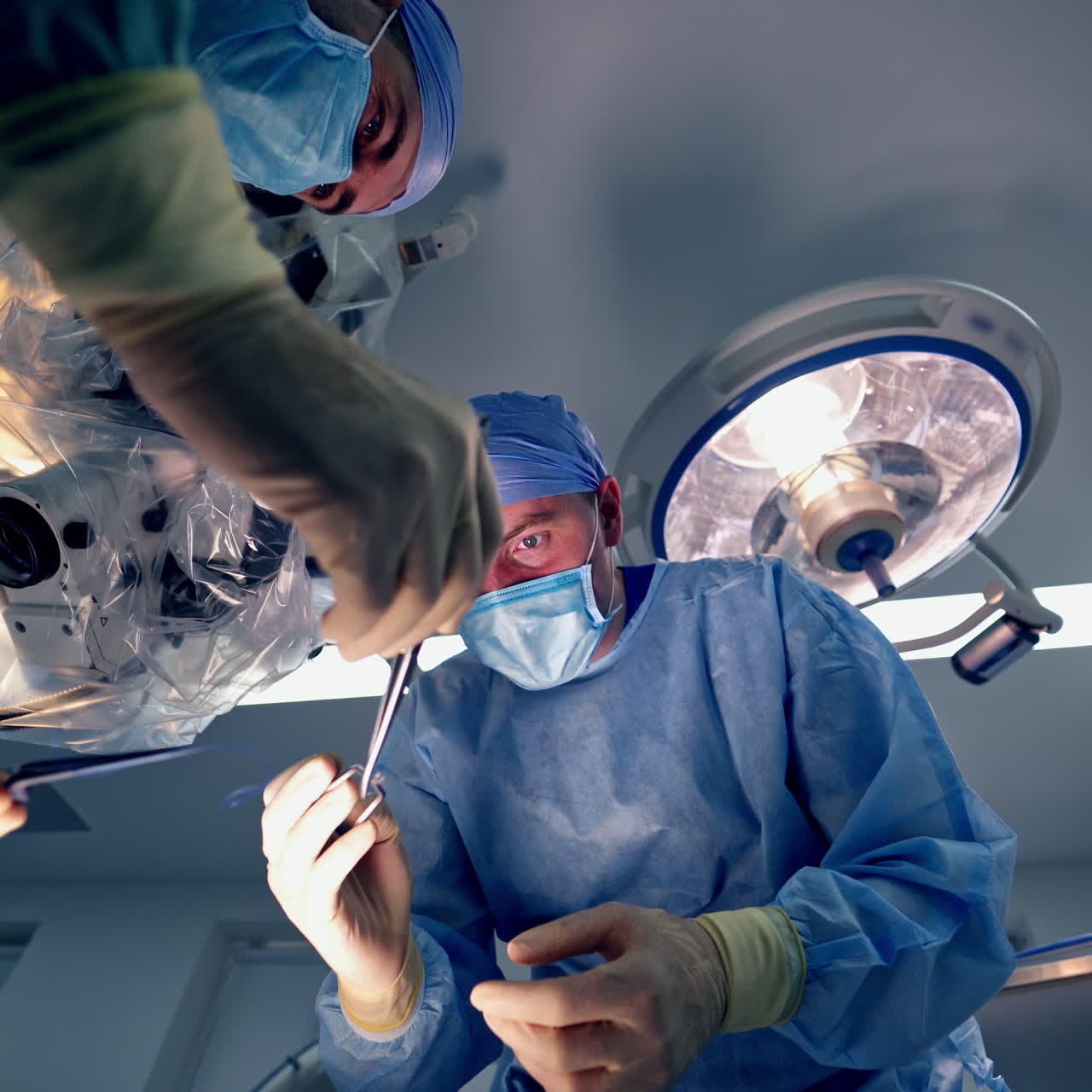 Surgeons with medical instruments. Doctors in medical uniform with masks perform surgery on modern equipment background in clinic. View from below.