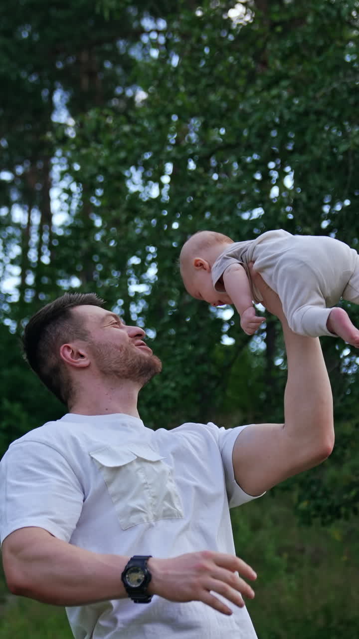 Muscular Caucasian man holding his newborn above head with one hand. Smiling happy dad entertaining his son. Nature backdrop. Vertical video