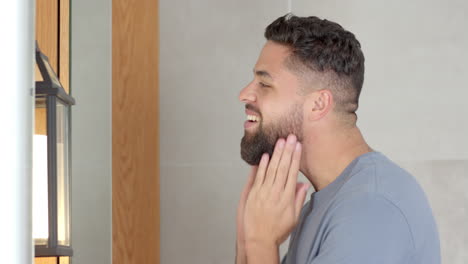 grooming beard, smiling man applying skincare product in bathroom mirror