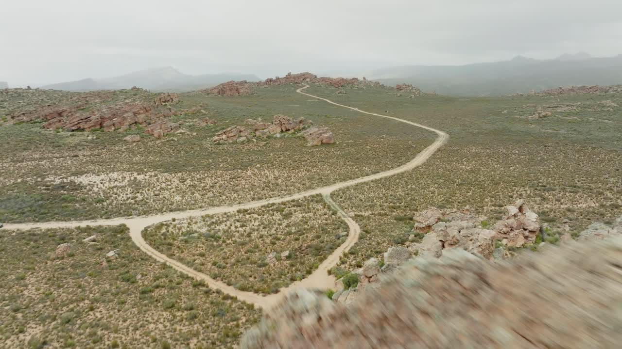 el dron vuela rápidamente sobre formaciones rocosas en el área silvestre de cederberg en sudáfrica con una amplia vista de la cordillera y el paisaje desértico con una carretera vacía.