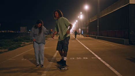 teen skaters riding skate boards enjoying night street. man balancing skateboard