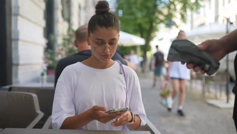 mujer joven pagando en una cafetería al aire libre con pago móvil