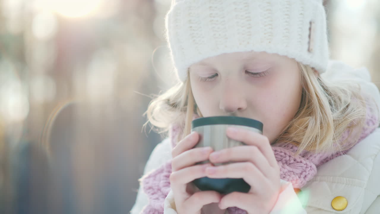 따뜻한 니트 모자를 쓴 어린 소녀는 t의 겨울 숲 초상화에 있는 보온병에서 뜨거운 차를 마신다