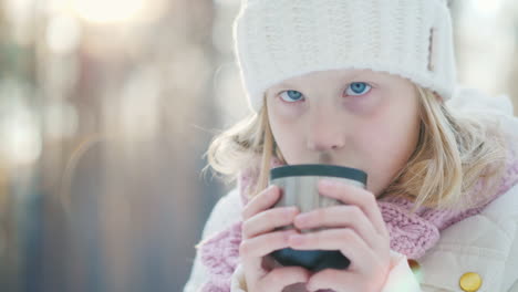 Ein-Kleines-Mädchen-In-Einer-Warmen-Strickmütze-Trinkt-Heißen-Tee-Aus-Einer-Thermoskanne-Im-Winterwaldporträt-In-T