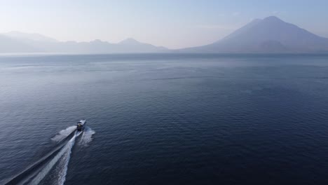 aerial follows tourism tour boat on lake atitlan, gtm volcano mountain