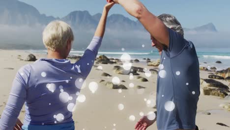 Happy-caucasian-senior-couple-dancing-on-beach,-over-moving-bokeh-light-spots