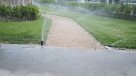 a sprinkler system watering a green lawn with a gravel path running through the middle