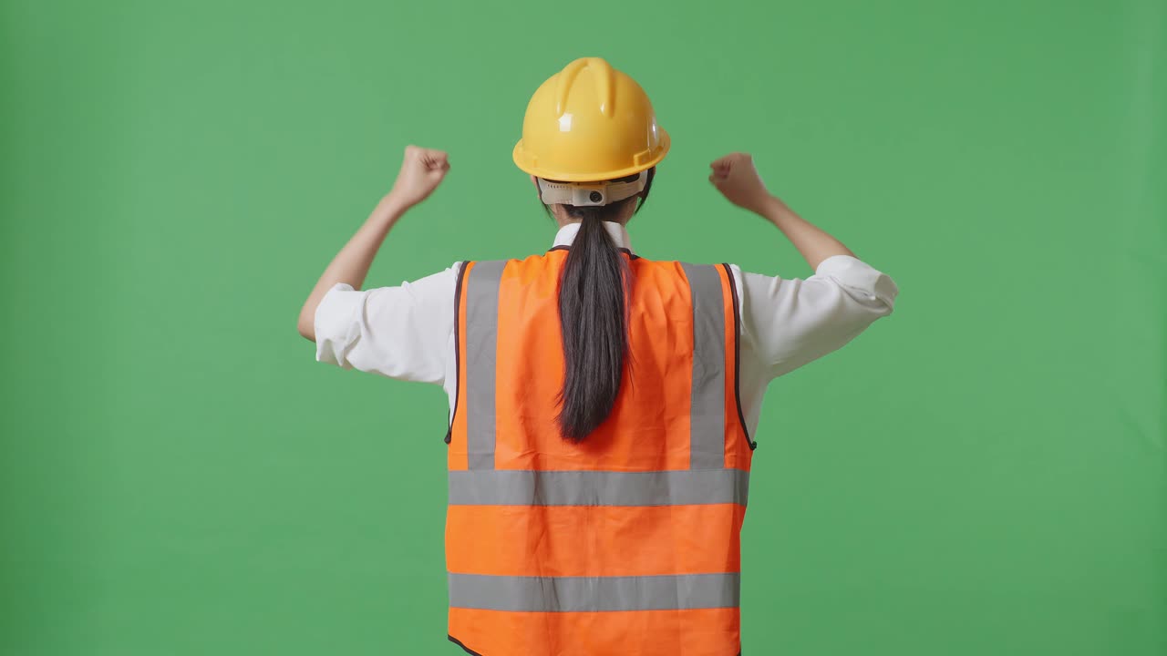안전 헬 을 착용 한 여성 엔지니어 가 녹색 스크린 배경 스튜디오 에서 일 하는 동안 손 을 들어 축하 하는 모습