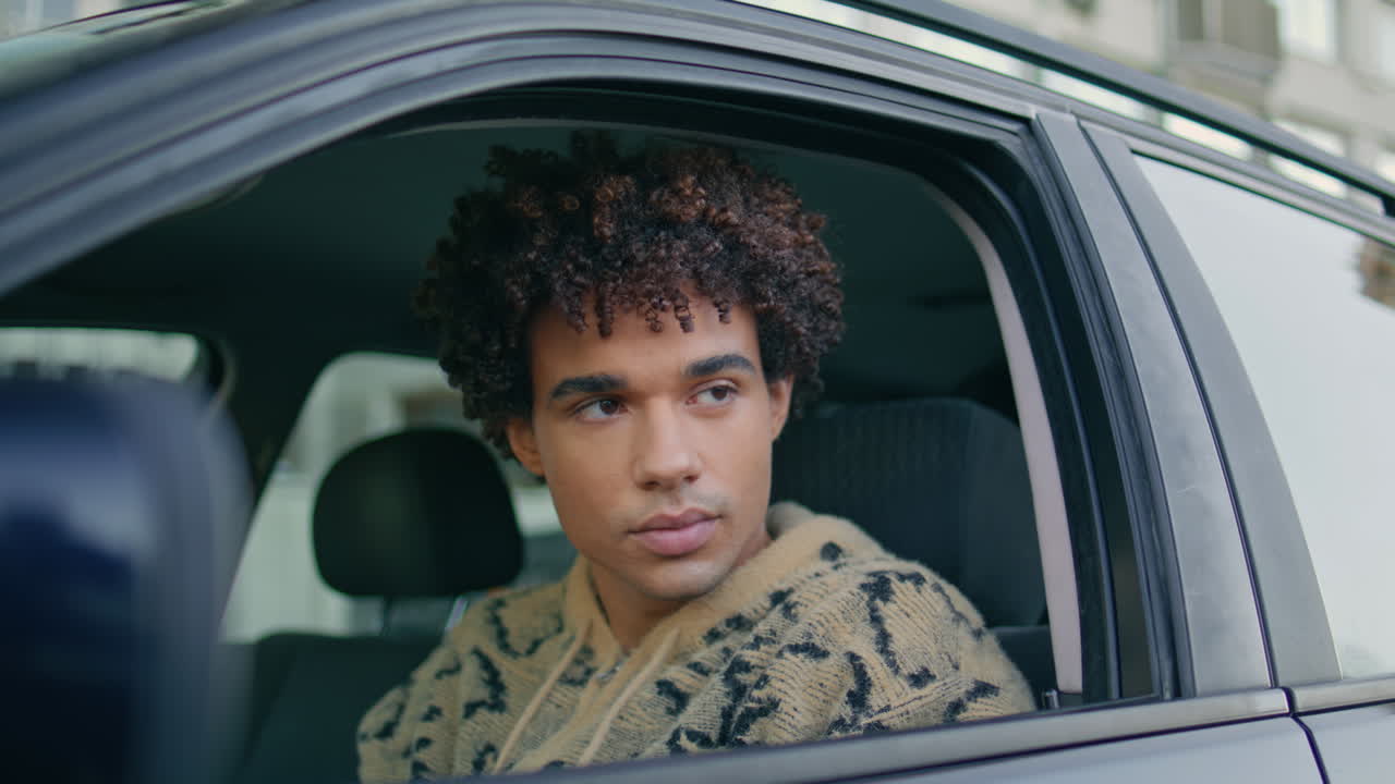 tío mirando el espejo del coche sentado en el asiento delantero de primer plano. conductor latino rizado esperando