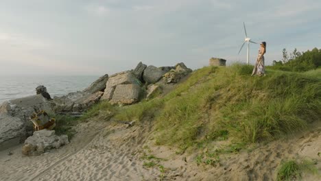 aerial establishing view of beautiful young romantic caucasian girl in a long dress on the white sand beach with old ruins, sunny summer evening, sunset, golden hour, wide drone shot moving forward