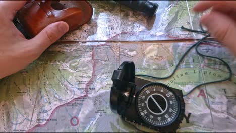 hitchiker preparing to hike on trail in mountains analyzing the map with a compass, pencil and knife, pov, first perspective