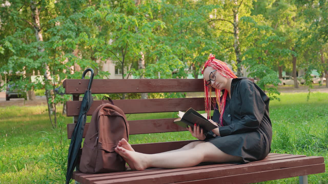 젊은 여성이 나무 아래에 앉아 책을 읽고 있어요. 한 여성이 자연 속에서 독서를 즐기고 있으며, 젊은 여성이 공원에서 휴식을 취하며 책에 몰두하고 있어요.