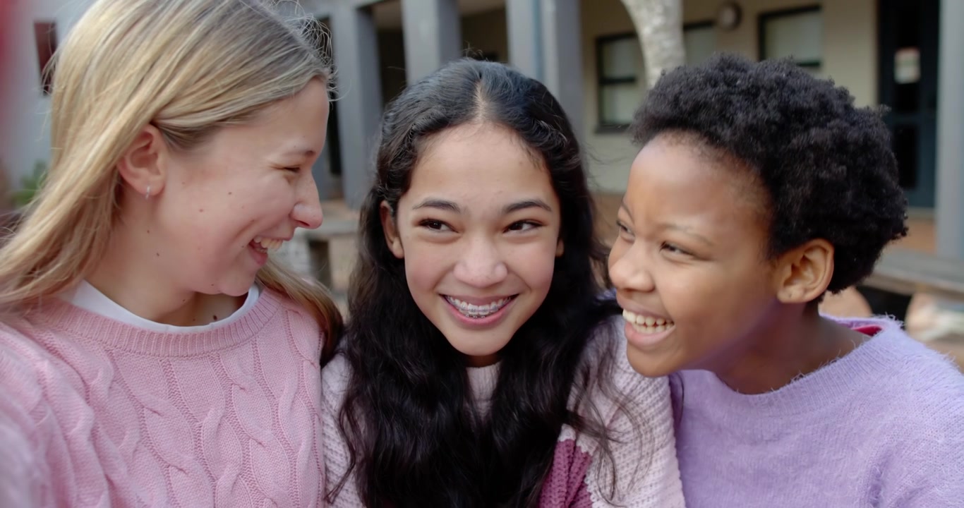 Diverse teenage female friends left girl holding phone taking selfie hugging braces on campus