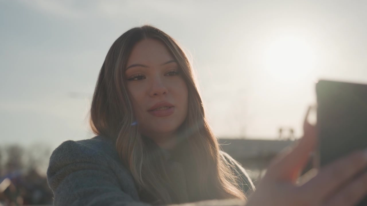 Outdoor city vlog. Woman outdoors films spontaneous city scenes with expressive gestures. Asian woman records natural city scenes outdoors during golden hour with expressive movements
