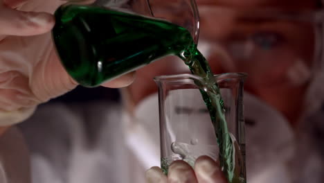 scientist pouring green liquid into beaker