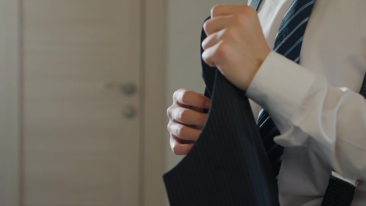 静かなアパートでサスペンダーとネクタイを整える男性。ベストを留め、シャツの袖口をなめらかにし、ストライプのネクタイを直す手のクローズアップ。質感のあるウールベストと清潔な白いシャツのディテールが雰囲気を強調している。
