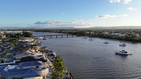 Drone footage captures luxury estates and boats along Gold Coast's river at sunset, showcasing serene waters and vibrant skies