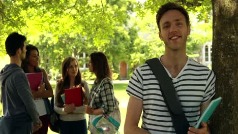 Cheerful-student-posing-and-classmates-speaking-behind-him