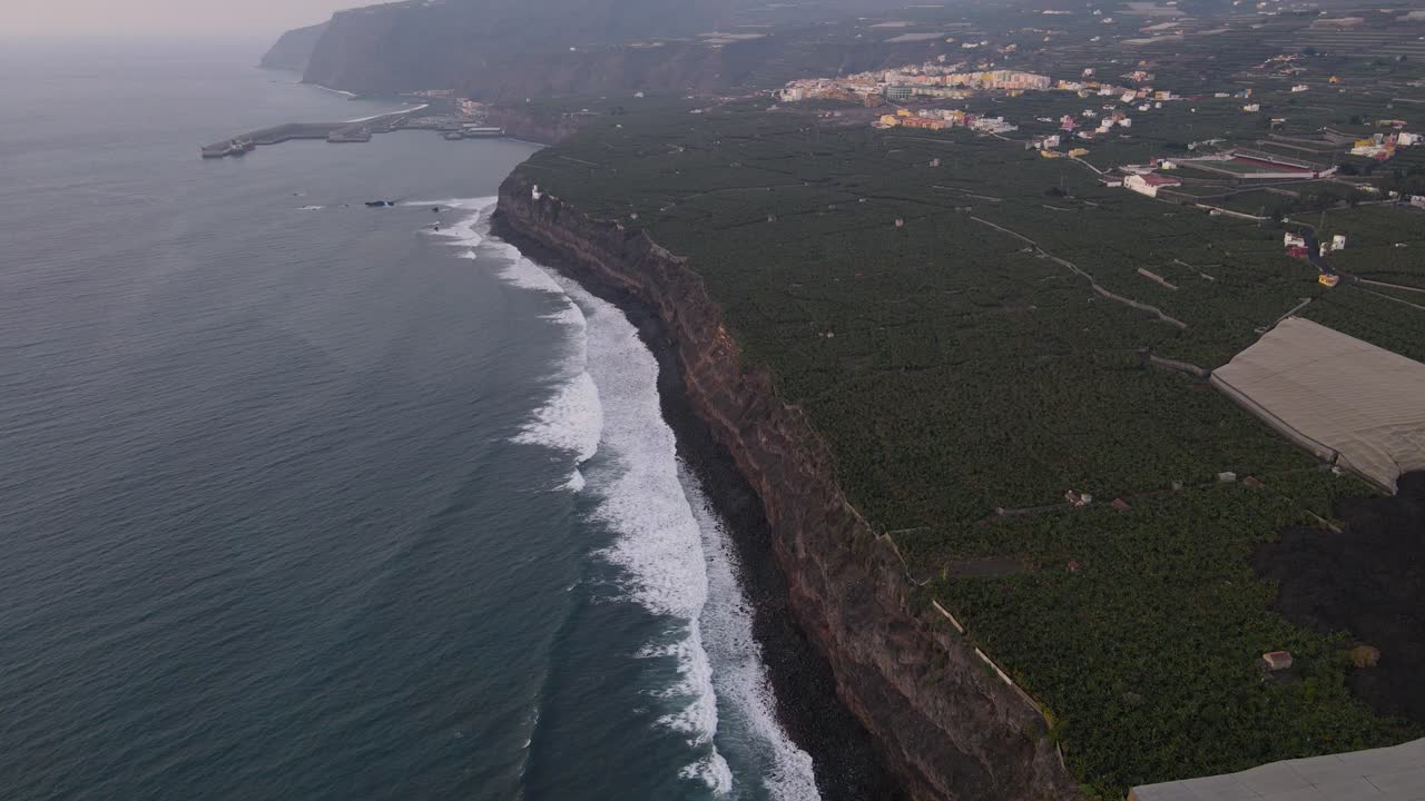 Ripresa aerea in avanti lungo scogliere con campi di piantagioni di banane invasi da lava solidificata, isola di La Palma