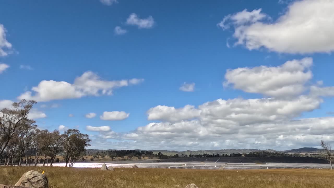 Nuvole cumulo veloci scivolano su un cielo azzurro brillante sopra un vasto campo rurale.