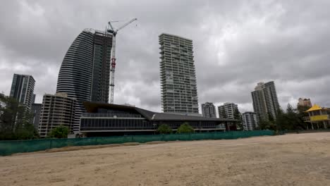 a stormy beach scene with strong winds and turbulent ocean waves under overcast skies, showcasing urban buildings in the background