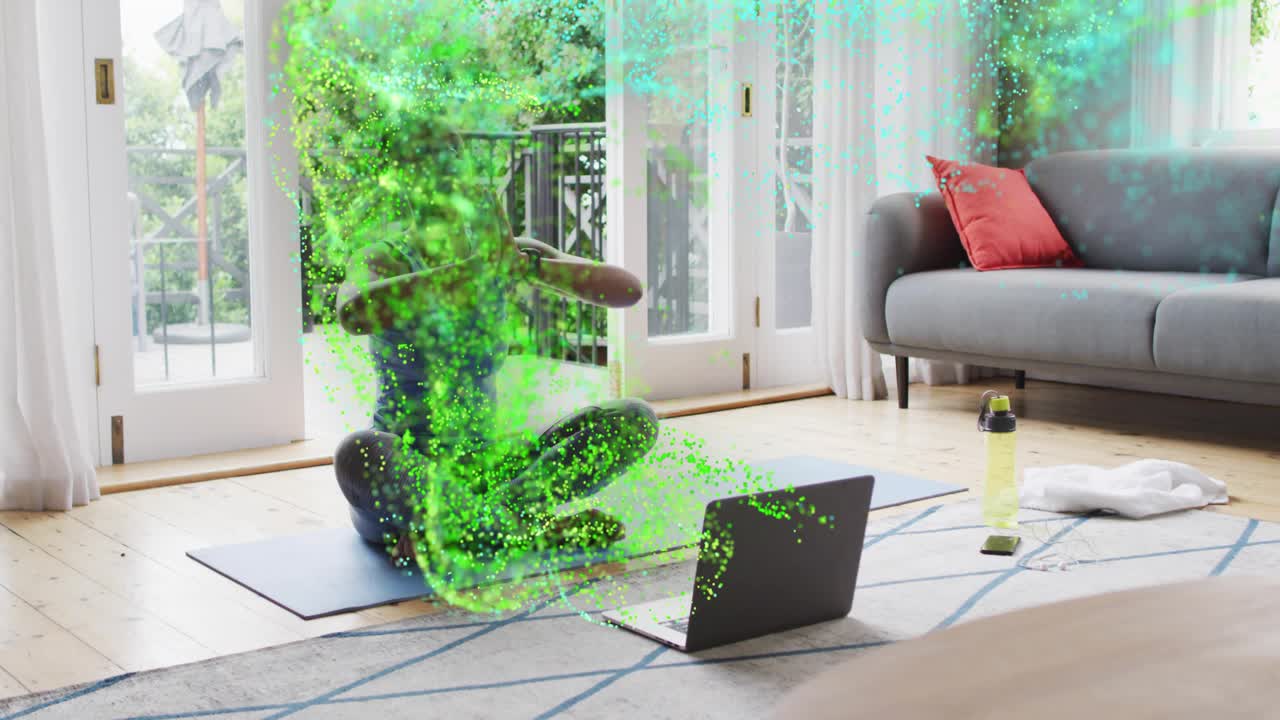 Woman practicing yoga on blue mat following laptop for wellness, green particles wrapping her