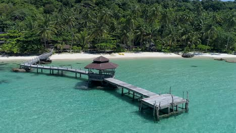 Drone-circling-around-wooden-footbridge-leading-into-the-sea