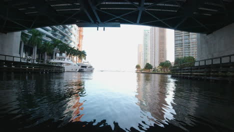 Vista-Desde-Un-Pequeño-Barco-Pasando-Por-Debajo-De-Un-Puente-En-Un-Estrecho-Canal-Bordeado-De-Yates-En-Miami,-Florida