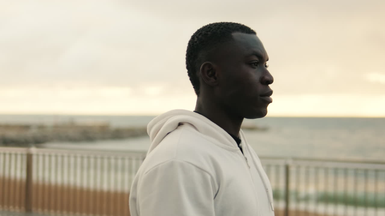 Thoughtful Young Man in White Hoodie Looking at the Ocean
