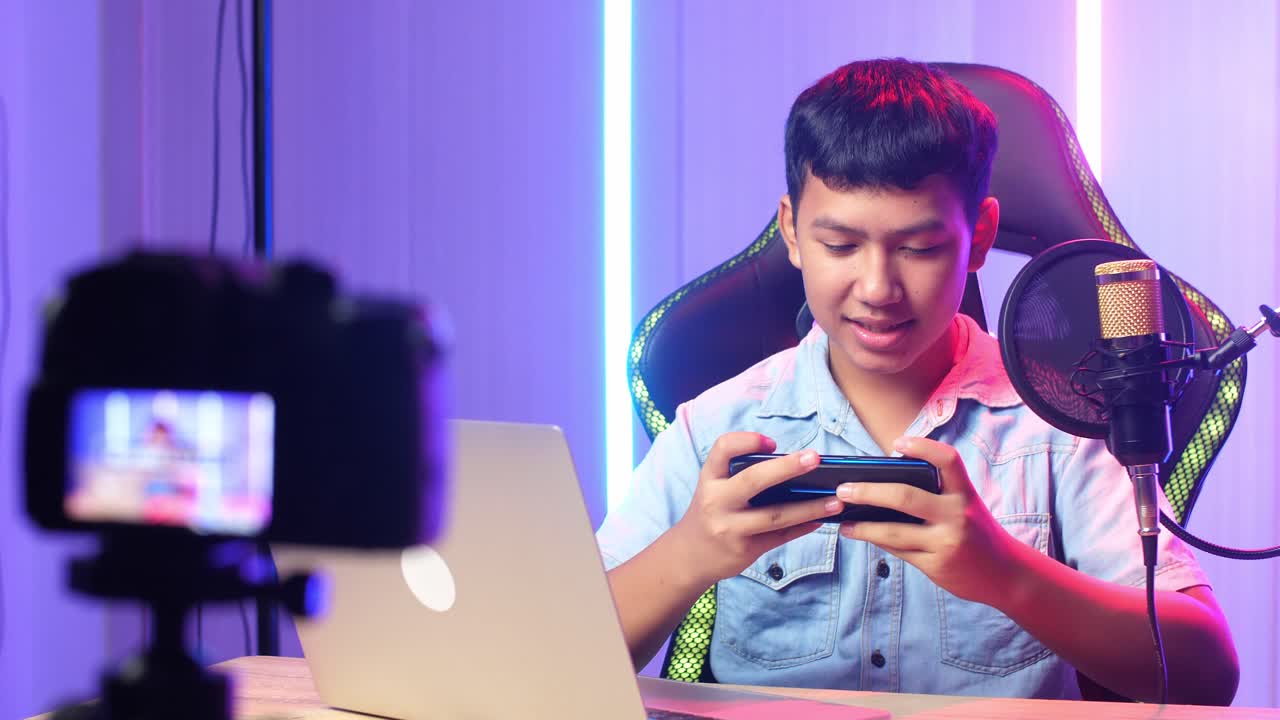 Bambino asiatico entusiasta che gioca a un videogioco con il telefono cellulare, poi sorride alla telecamera durante una diretta streaming.