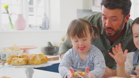 father with down syndrome daughter baking and decorating cakes sitting around table at home