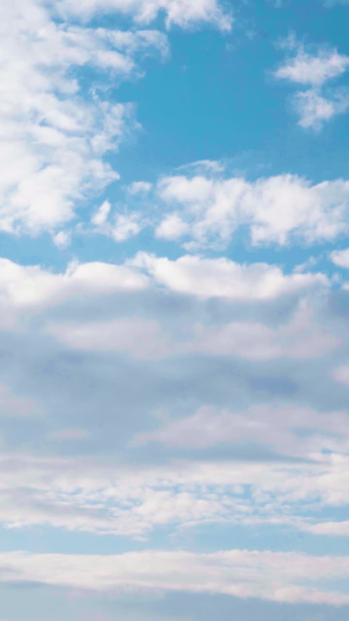 Vertical video of calm blue sky with slow-moving fluffy clouds. Ideal as a relaxing natural background or seamless wallpaper for peaceful and airy visual content.