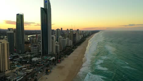 Paraíso-De-Los-Surfistas-Al-Atardecer,-Edificios-De-Gran-Altura,-Olas-Rompiendo-En-Playas-Doradas