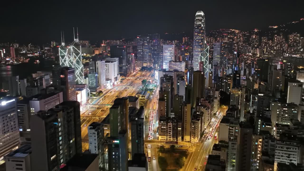 Bright city lights illuminate the bustling streets of Hong Kong as tall skyscrapers rise against the night sky. The skyline reflects the vibrancy and energy of this urban landscape.