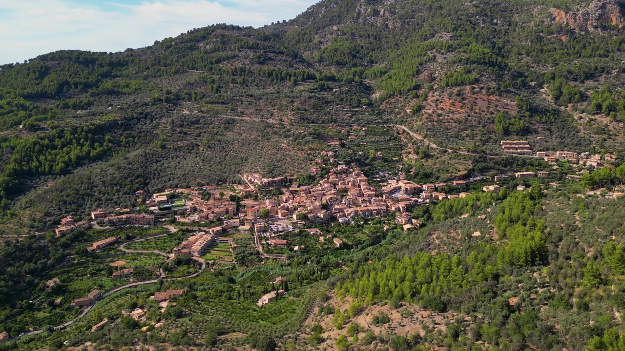 Veduta aerea di Fornalutx, un pittoresco villaggio incastonato tra le montagne della Tramuntana sull'isola di Maiorca, Spagna, che mostra l'architettura tradizionale e la vegetazione lussureggiante, ripresa aerea grandangolare con drone in orbita