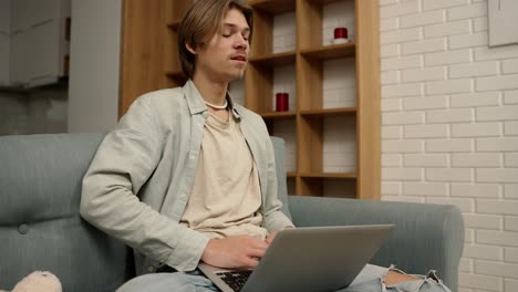 Young-man-sitting-on-sofa-working-from-home-on-laptop