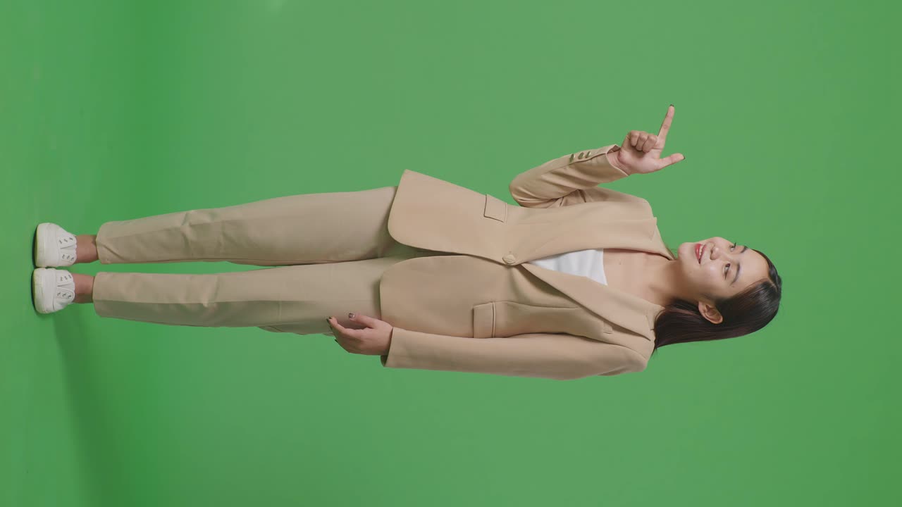 녹색 스크린에 서 있는 동안 을 가리키는 미소를 가진 아시아 사업가 여성의 전체 몸