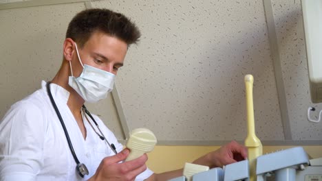 young doctor in protective mask working on ultrasound device. doctor adjusts the ultrasound device
